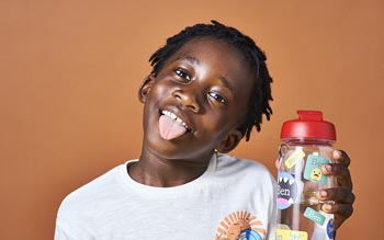 Boy holding a water bottle with waterproof name stickers from My Nametags, on a brown background