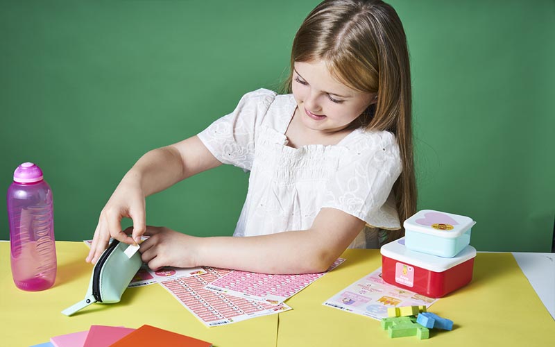 Girl showing how easy our name stickers are to use by putting them on a pencil case