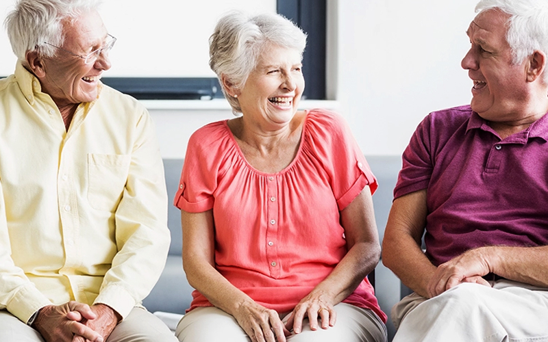 Multiple seniors talking to eachother and laughing, on a grey and white background