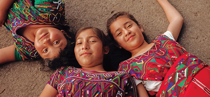 Three girls lying on the ground, smiling and enjoying a sunny day outdoors