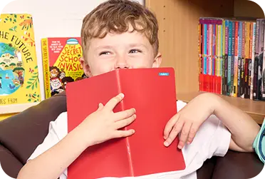 Little boy holding book in front his face. Book has a ministicker label on it.